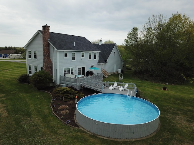 rear view of house featuring a lawn, roof with shingles, an outdoor pool, a wooden deck, and a chimney