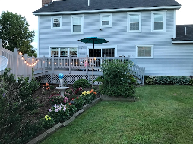 back of property with a lawn, a deck, a chimney, and a shingled roof