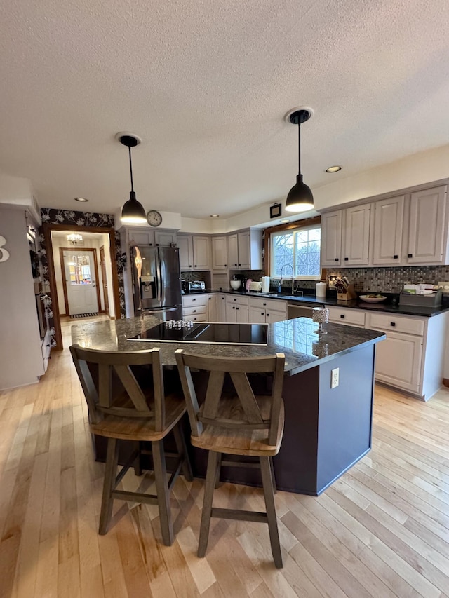 kitchen with dark countertops, a center island, light wood-type flooring, and stainless steel fridge with ice dispenser