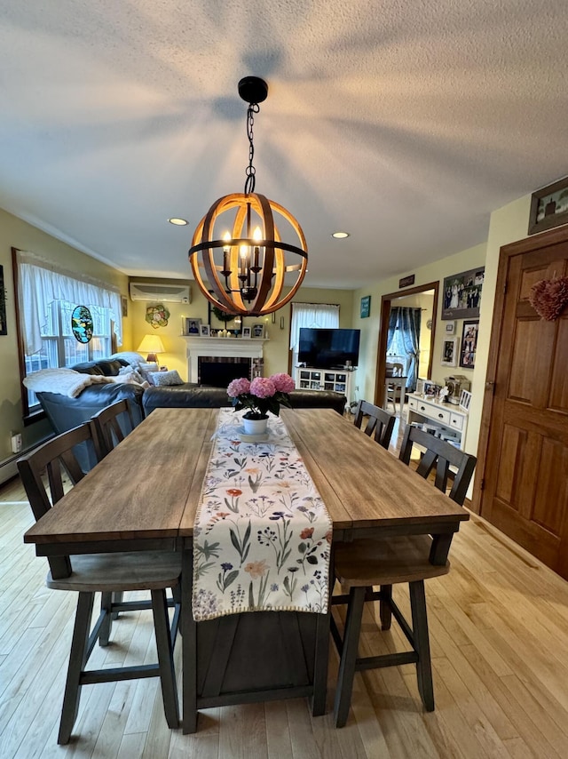 dining area featuring a chandelier, a fireplace, a textured ceiling, and light wood-style floors