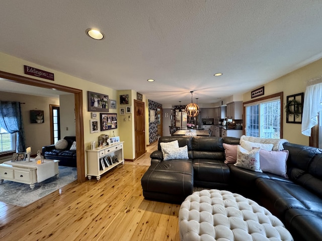 living room featuring light wood-type flooring, a notable chandelier, a healthy amount of sunlight, and a textured ceiling