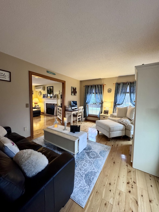 living room with light wood-style flooring, a fireplace, a textured ceiling, and a wall unit AC