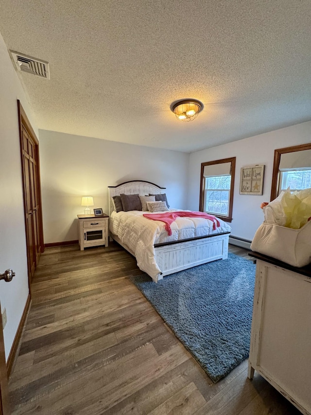 bedroom featuring visible vents, multiple windows, wood finished floors, and a baseboard radiator