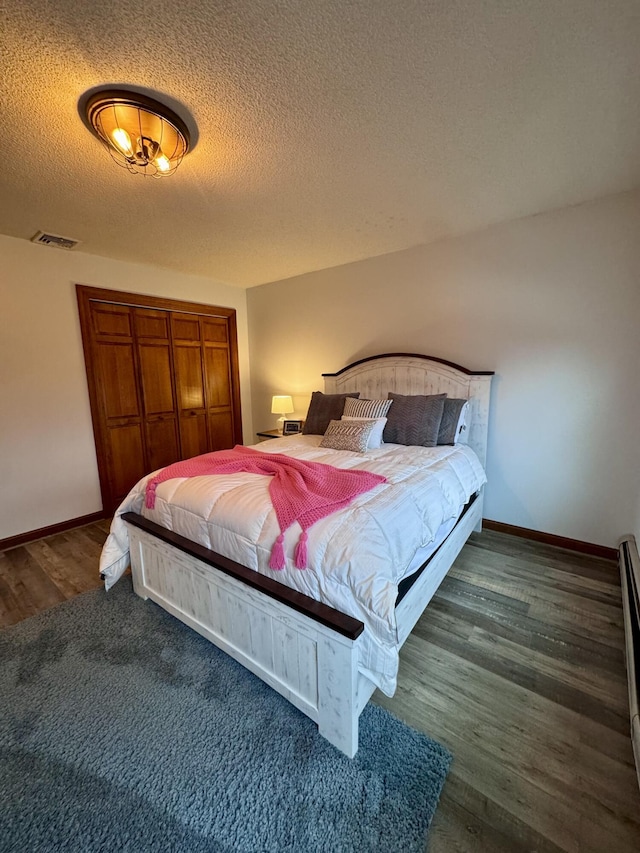 bedroom featuring baseboards, wood finished floors, visible vents, and a textured ceiling