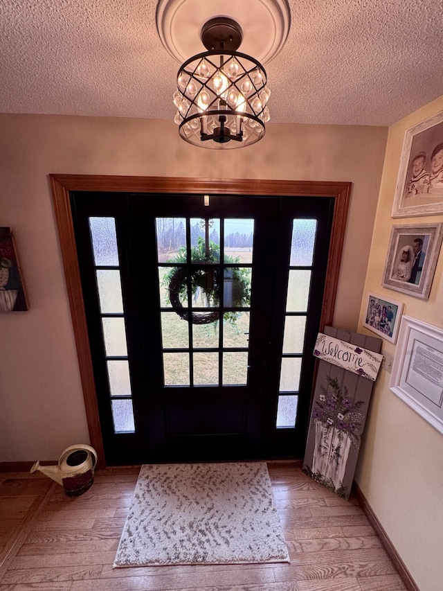 foyer entrance with a notable chandelier, a textured ceiling, baseboards, and light wood-style floors