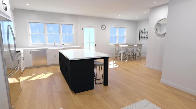 kitchen with a kitchen breakfast bar, a center island, light countertops, freestanding refrigerator, and light wood finished floors