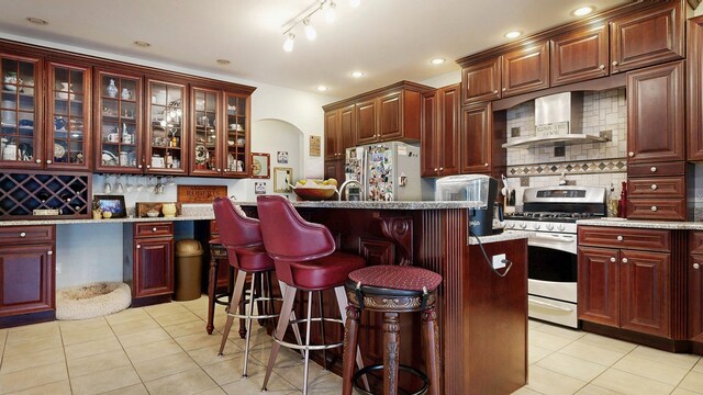 16 Ocean Greens Dr, Saco, ME 04072 - kitchen with reddish brown cabinets, wall chimney exhaust hood, arched walkways, and stainless steel appliances