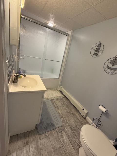 16 Ocean Greens Dr, Saco, ME 04072 - full bath featuring combined bath / shower with glass door, wood finished floors, toilet, vanity, and a paneled ceiling