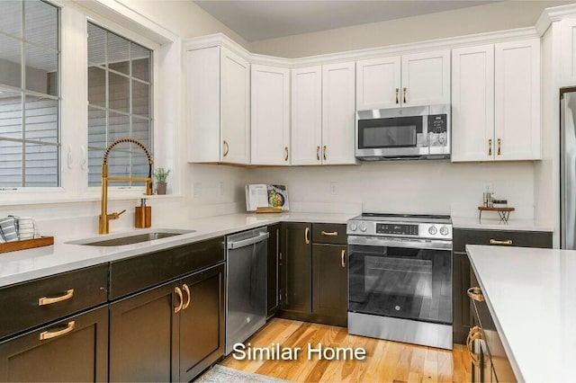 kitchen with a sink, appliances with stainless steel finishes, white cabinets, and light countertops