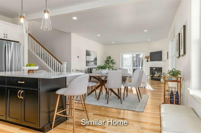 dining room featuring a glass covered fireplace, recessed lighting, stairway, and light wood-type flooring