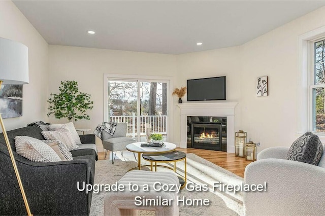 living room with a wealth of natural light, a glass covered fireplace, wood finished floors, and recessed lighting