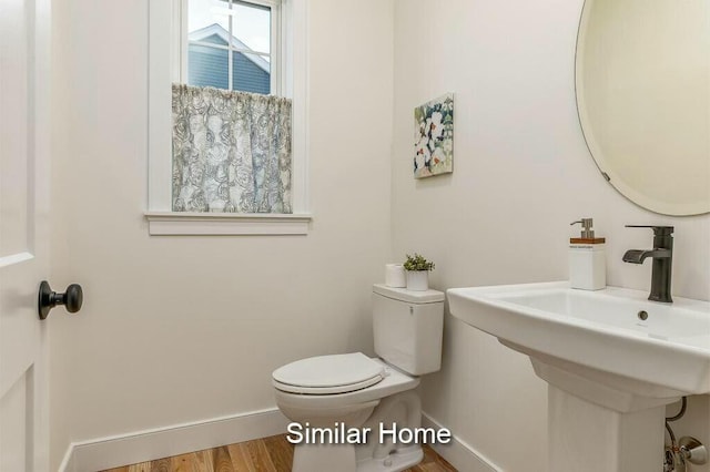 half bath with a sink, baseboards, toilet, and wood finished floors