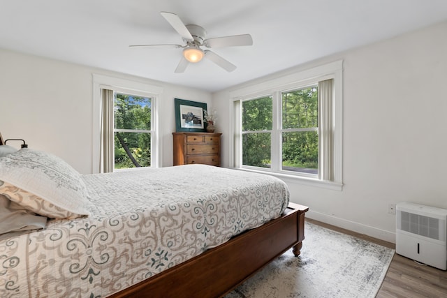 bedroom featuring a ceiling fan, baseboards, multiple windows, and wood finished floors