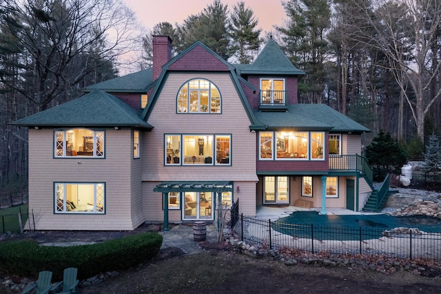 8 Spruce Point Rd, Kittery, ME 03904 - back of house at dusk featuring stairs, a patio, a fenced backyard, a balcony, and a chimney