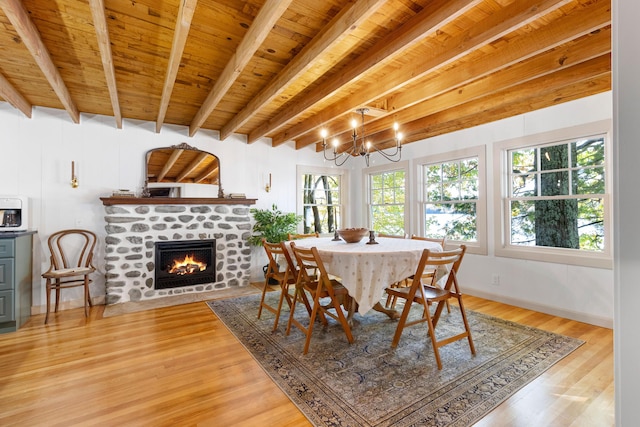 dining space featuring a notable chandelier, light wood finished floors, a glass covered fireplace, beamed ceiling, and wood ceiling