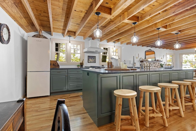 kitchen with freestanding refrigerator, dark countertops, custom exhaust hood, and wood ceiling
