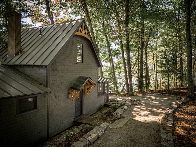 view of side of property with a standing seam roof, a chimney, and metal roof