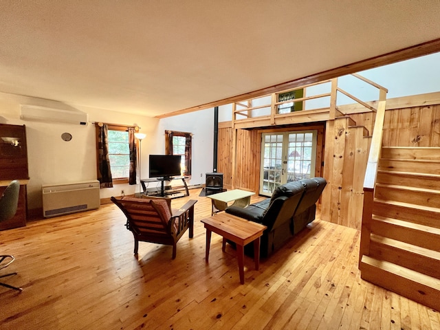 living room featuring a wall mounted air conditioner, a wood stove, stairway, and light wood-style flooring