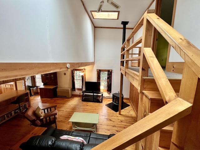 living room featuring wood-type flooring, crown molding, a wood stove, and a high ceiling