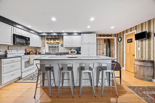 663 Eastbrook Rd, Eastbrook, ME 04634 - kitchen featuring black microwave, white electric stove, white cabinets, a breakfast bar, and a kitchen island