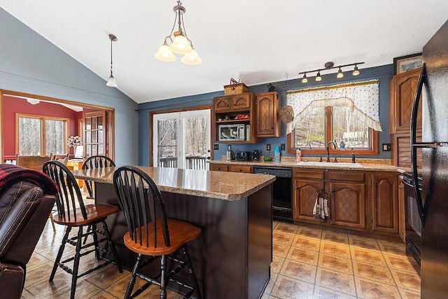 kitchen featuring black appliances, a sink, a kitchen breakfast bar, a kitchen island, and vaulted ceiling