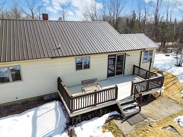 snow covered property with a chimney, a wooden deck, and metal roof