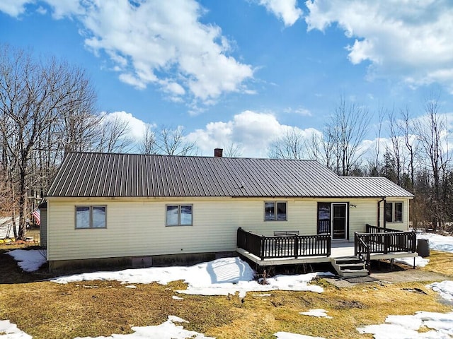 snow covered back of property with metal roof, a deck, and a chimney