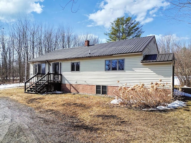 back of house with a chimney and metal roof