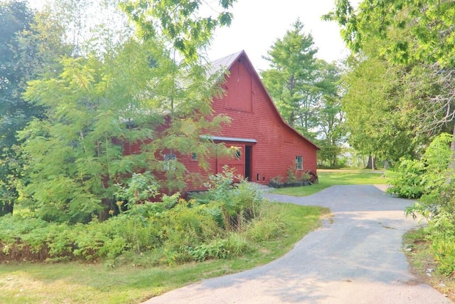 view of home's exterior with a yard, a barn, and driveway