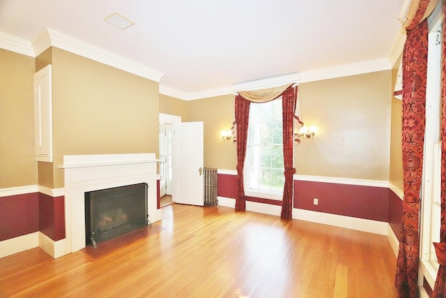 unfurnished living room with wood finished floors, radiator, a fireplace, crown molding, and baseboards