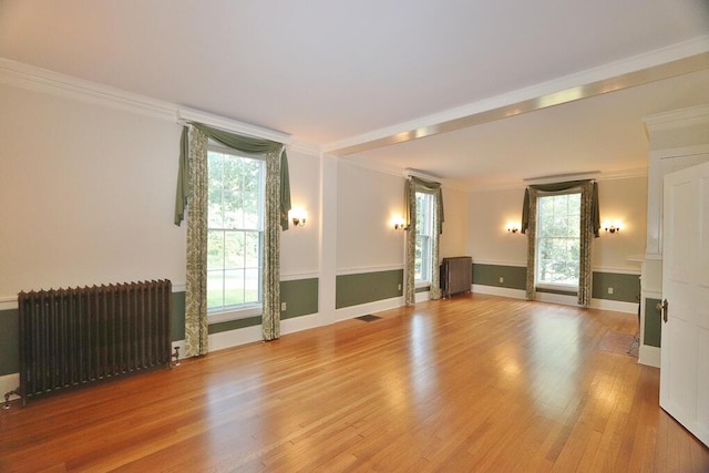 unfurnished living room with wood finished floors, baseboards, radiator heating unit, a fireplace with flush hearth, and crown molding