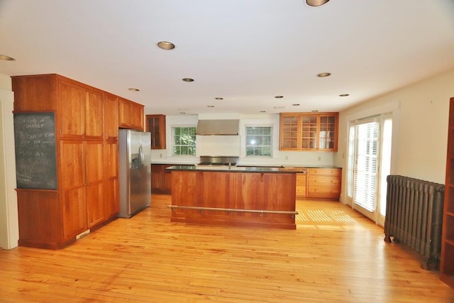 kitchen featuring light wood finished floors, stainless steel fridge, radiator heating unit, and wall chimney range hood