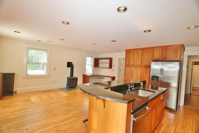 kitchen with radiator, dark stone countertops, stainless steel refrigerator with ice dispenser, brown cabinetry, and a sink