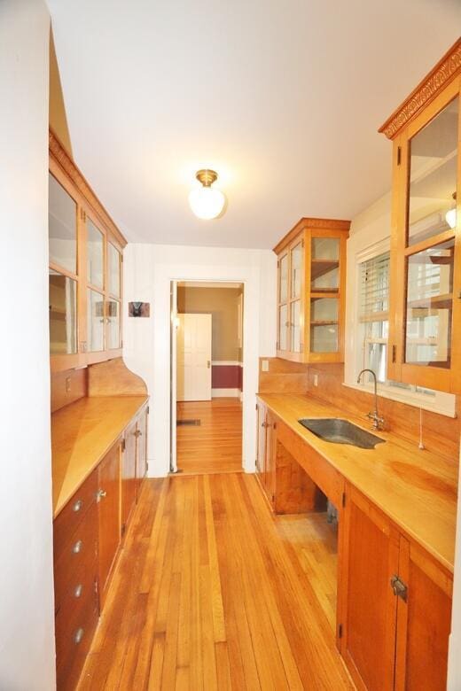 kitchen with glass insert cabinets, light wood-style floors, and a sink