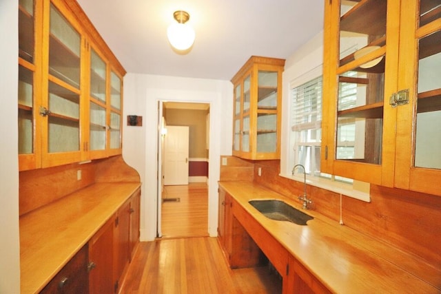 kitchen featuring light wood-style flooring, decorative backsplash, a sink, light countertops, and glass insert cabinets