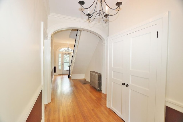 hallway featuring light wood finished floors, radiator heating unit, ornamental molding, arched walkways, and a notable chandelier