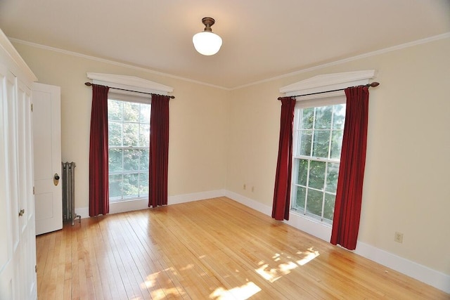 spare room featuring hardwood / wood-style floors, crown molding, baseboards, and a wealth of natural light
