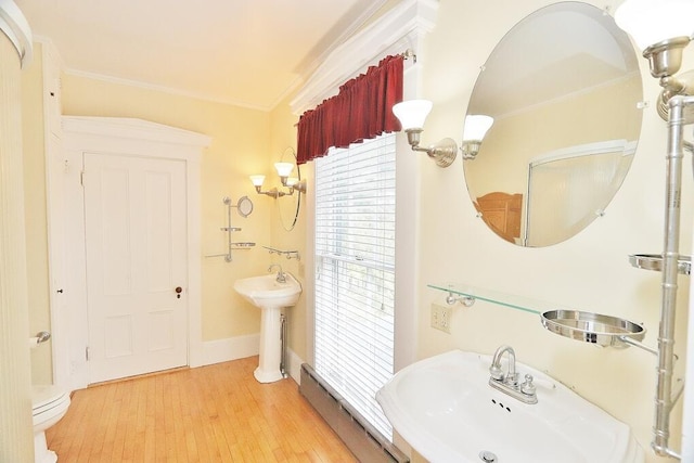 bathroom with a sink, baseboards, wood finished floors, and ornamental molding