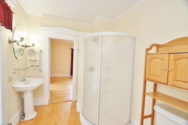 bathroom with wood finished floors, toilet, ornamental molding, and a shower stall