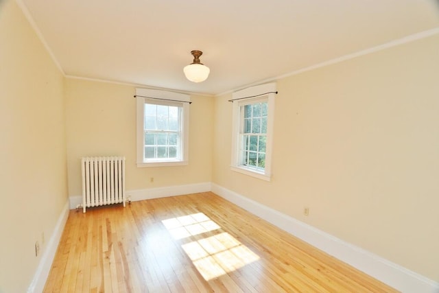 spare room with radiator heating unit, baseboards, light wood finished floors, and ornamental molding