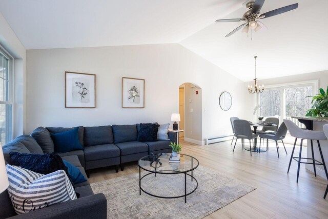 living area featuring light wood finished floors, arched walkways, vaulted ceiling, ceiling fan with notable chandelier, and a baseboard radiator