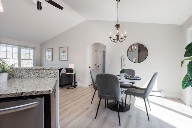 dining area with light wood finished floors, vaulted ceiling, arched walkways, baseboards, and ceiling fan with notable chandelier