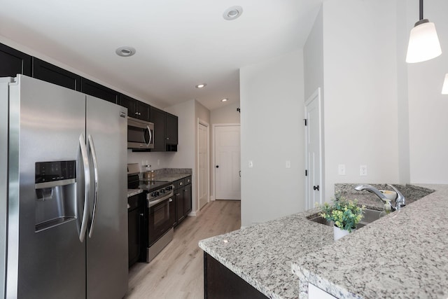 kitchen with stainless steel appliances, light wood-style flooring, a sink, dark cabinetry, and light stone counters