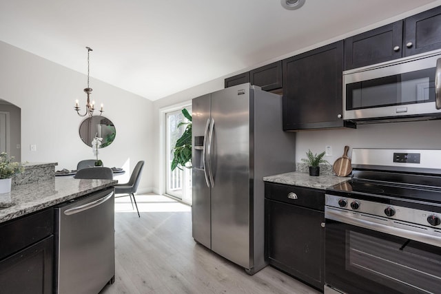 kitchen with vaulted ceiling, light wood-style floors, stainless steel appliances, a notable chandelier, and light stone countertops