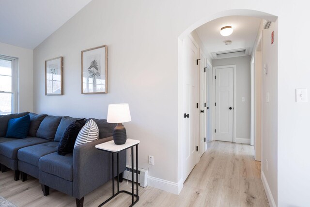 interior space with vaulted ceiling, arched walkways, baseboards, a baseboard radiator, and light wood-style flooring