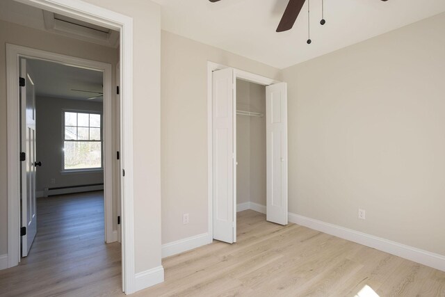 unfurnished bedroom featuring a baseboard radiator, baseboards, wood finished floors, and a closet