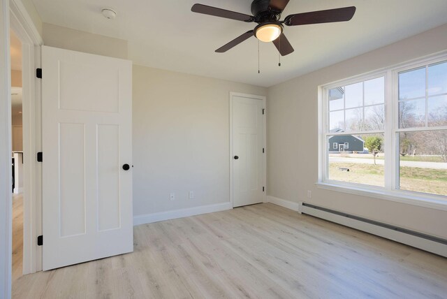 empty room featuring a baseboard radiator, baseboards, ceiling fan, and light wood finished floors