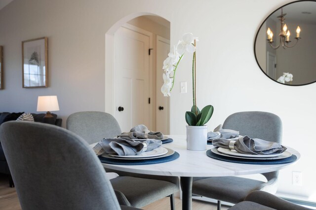 dining space with wood finished floors, arched walkways, and a notable chandelier