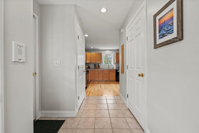 corridor featuring recessed lighting, light tile patterned flooring, baseboards, and a sink