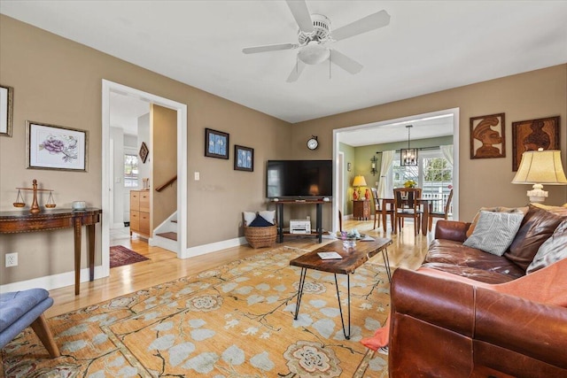 living room with stairway, light wood-type flooring, a ceiling fan, baseboards, and a chandelier